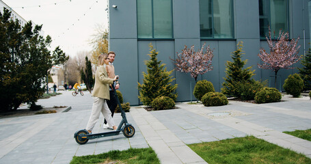 Two smiling colleagues going downtown street talking. Office managers commuting to work with eco-friendly vehicles. Technology, partnership, occupation concept. © serg