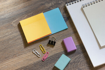 Notebooks with a pen, colored note paper, erasers and paper clips on a wooden table