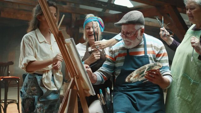 Old man artist and his friends celebrate finishing painting on canvas with oil paints and brush In the art studio