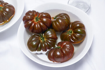 Juicy tomatoes in a white bowl of water on a white background. Fresh red tomatoes in different colors in a bowl. Selective focus.Top view.