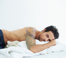 Fototapeta na wymiar Thinking, relax and topless with a sexy man on a bed, lying in studio on a white background. Tattoo, idea and shirtless with a handsome young male model posing in a bedroom for sensuality or desire