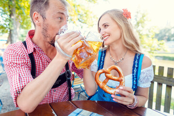 Woman and man enjoying the beer garden in Tracht - obrazy, fototapety, plakaty