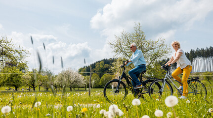 Senior coSenior couple riding bicycles in spring through a meadowuple riding bicycles in spring - 602591329