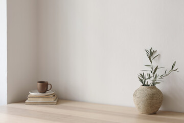Neutral Mediterranean home design. Textured vase with olive tree branches, cup of coffee. Books on...