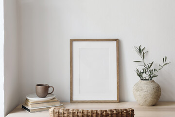Closeup of picture frame, poster mockup. Vase with olive tree branches on wooden table. Blurred...