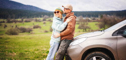 Romantic happy middle age couple hugging standing next to cars during auto travel in mountains