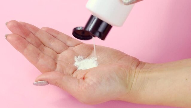 White enzyme powder pouring into the Caucasian woman hand from the bottle close up. Skin care and facial cleansing