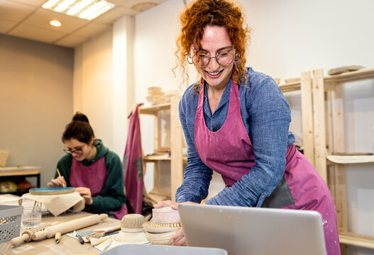 Female business owner using laptop in pottery studio workshop.