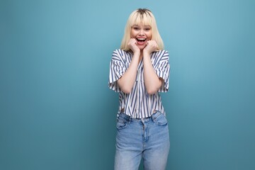 happy blond young woman in shirt rejoices on studio background with copy space