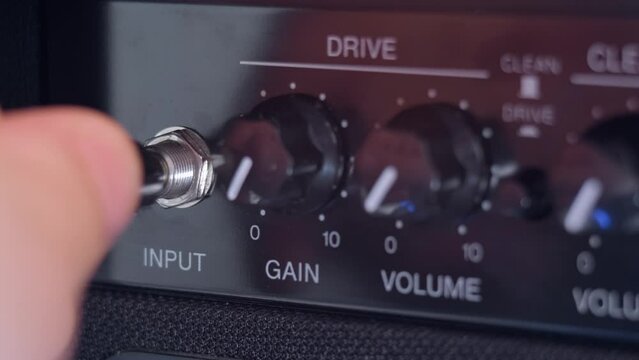 Guitarist plugs cable jack into the guitar amplifier. Amplifier receiver. Plugging jack to amp equipment. Macro footage.