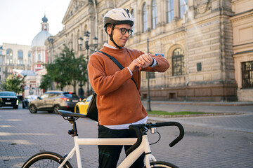 A punctual cyclist in a helmet looks at the clock of a young guy and a white bicycle riding to work...