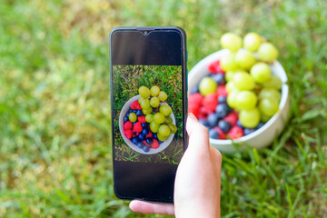 Fotografowanie telefonem komórkowym miski pełnej owoców leżącej na trawie 