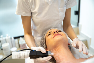 Closeup portrait of smiling female patient enjoying rejuvenation procedure performed by a beautician in a beauty clinic