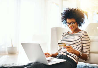 Young woman, laptop and credit card while doing online shopping sitting on ground. Home, happiness and computer internet deal of African female person on an ecommerce app reading banking details