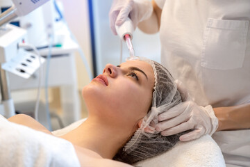 Obraz na płótnie Canvas Close up of young woman receiving electric darsonval facial massage after procedure at beauty clinic.