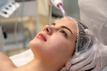 Close up of young woman receiving electric darsonval facial massage after procedure at beauty...