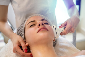 Obraz na płótnie Canvas Close up of young woman receiving electric ultrusound facial massage at beauty salon.