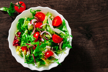 various fresh mix salad leaves with tomato in bowl on wooden background. with copy space. top view