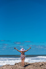 Happy and carefree woman standing with her arms open on the rocks near the sea.