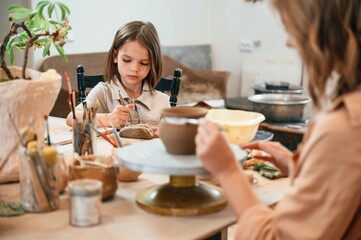 Painting the product. Mother with little girl making ceramic pot at home