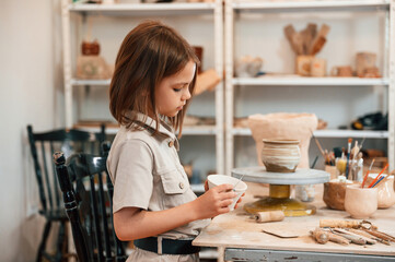 Side view. Little girl is indoors with ceramic pot in hands