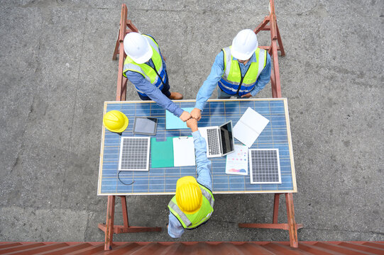 Top view of engineering team wearing helmets and safety vests discussion and brainstorming meeting for solar photovoltaic cell project. agreement for green alternative energy concept.