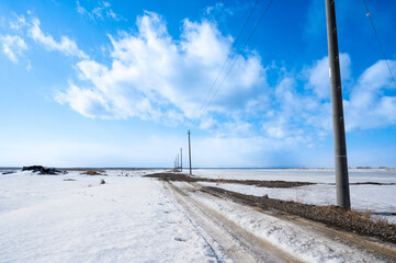 野付半島の雪が積もる大地にて、青い空と大地に通る一本道