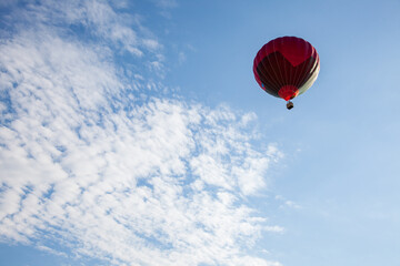 a red hot air balloon flying in a blue sky with white clouds