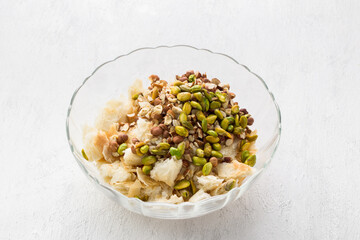 A glass bowl with pieces of puff pastry and nuts (hazelnuts, almonds and pistachios) for a delicious arabic umm ali dessert or other dish on a light gray background. Cooking stage