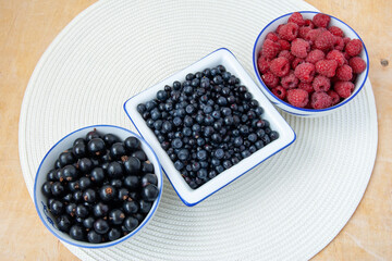 Three bowls with seasonal berries, a mix of fresh berries on a on a white round napkin on a wooden table, blueberries, currants, blueberries, raspberries