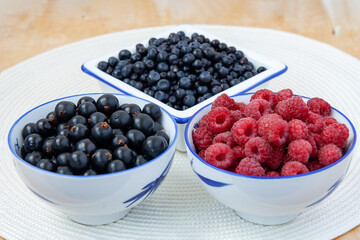 Three bowls with seasonal berries, a mix of fresh berries on a on a white round napkin on a wooden table, blueberries, currants, blueberries, raspberries