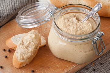 Fresh homemade mushroom pate in a jar and on a baguette slice on a rustic background, with...