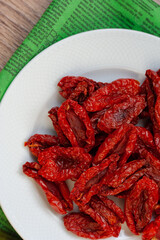 Sun-dried tomatoes with on a white plate, green napkin, wooden table