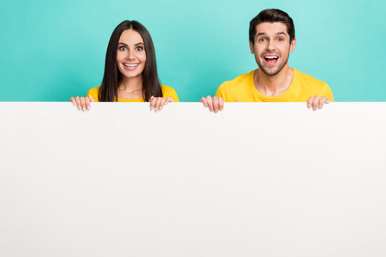 Photo of impressed funny husband wife dressed yellow t-shirts rising poster empty space isolated turquoise color background