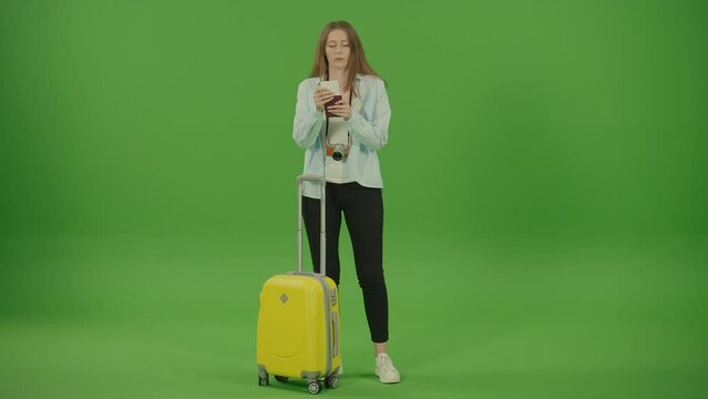 Green Screen. Chroma Key. Pretty Woman Tourist With Yellow Luggage in the Hands Passing by in Hurry, Checking Tickets, and Looking for Something. Woman Tourist With Camera on the Neck is Focused.