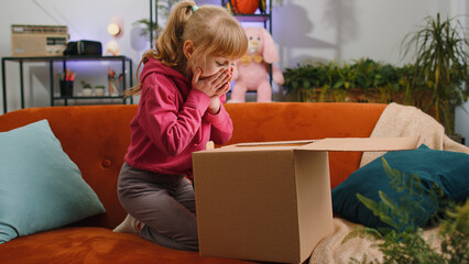 Happy young blonde child kid girl unpacking delivery parcel. Smiling satisfied teen toddler...