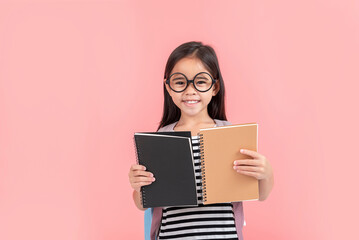 schoolgirl hugging book wearing backpack smiling isolated on pink background
