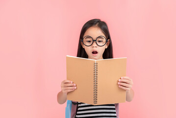 schoolgirl hugging book wearing backpack smiling isolated on pink background