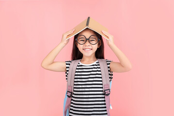 schoolgirl hugging book wearing backpack smiling isolated on pink background