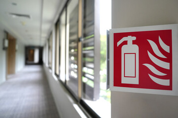 Close-up image features an emergency sign of a fire extinguisher in a building corridor. The image has a selective focus, drawing attention to the fire extinguisher sign.