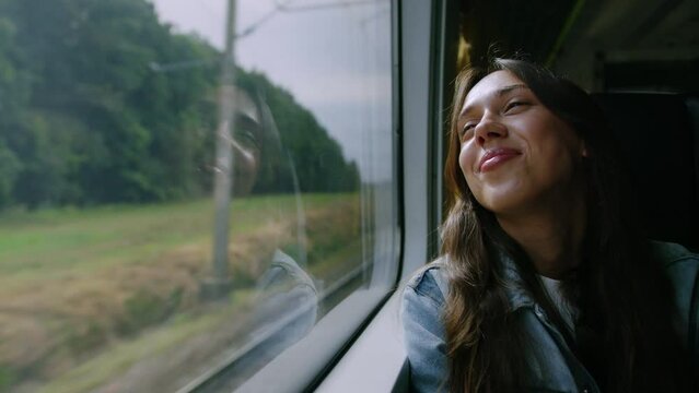 A woman enjoys a train ride. The brunette smiles and looks out the window