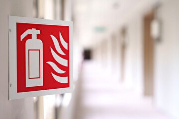 Close-up image features an emergency sign of a fire extinguisher in a building corridor. The image...