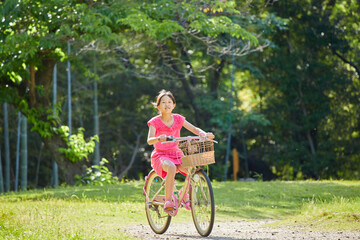 夏の公園で元気で自転車を乗って遊んでいる小学生の女の子の様子 - obrazy, fototapety, plakaty