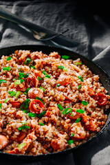 Fried Meat sausages in a frying pan with buckwheat porridge on dark wooden table