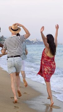 Young friends having fun running on the beach near the sea at sunset. Lifestyle travel holiday vacation in summer - vertical video