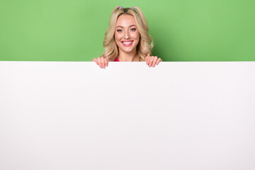 Photo of cheerful excited woman smiling holding white placard emtpy space isolated green color background
