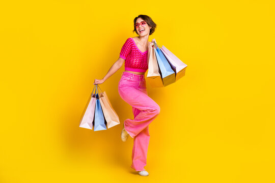 Full size photo of pretty girl knit top pink pants hold shopping bags look at sale empty space dancing isolated on yellow color background