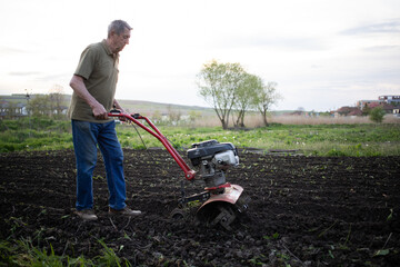 man cultivates the ground in the garden with a tiller preparing the soil for sowing