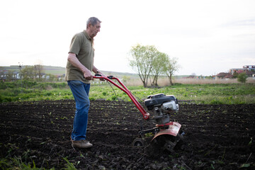 man cultivates the ground in the garden with a tiller preparing the soil for sowing