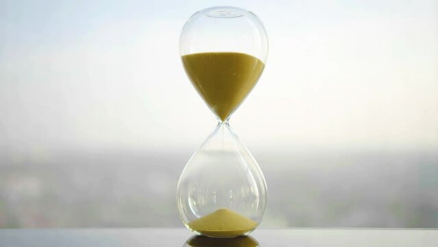 hourglass on table, sand flowing through the bulb of sandglass, time is money concept, times passing concept like work or business deadline, resemble urgency running out of occasion in life